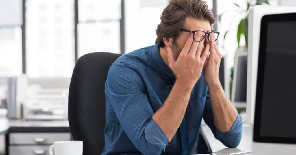 A man with glasses covering his face in front of a computer, potentially contacted by collection agencies.