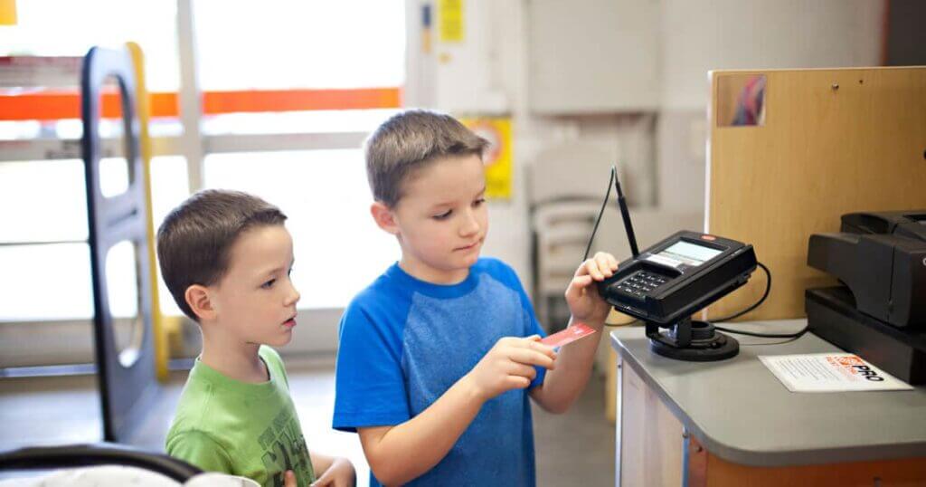 Two children mastering the art of using a credit card machine in a store.