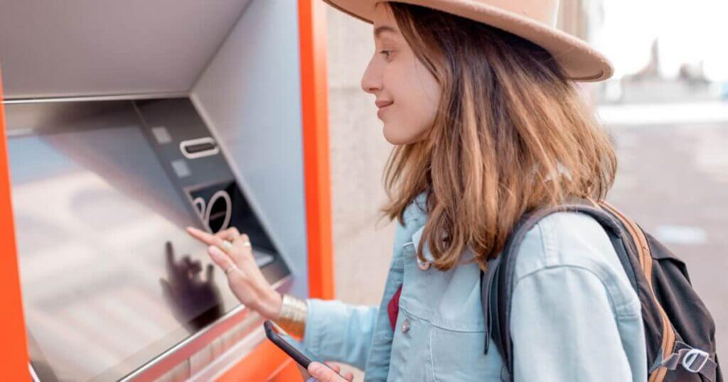 A woman is withdrawing cash from an ATM while being mindful of ATM fees.